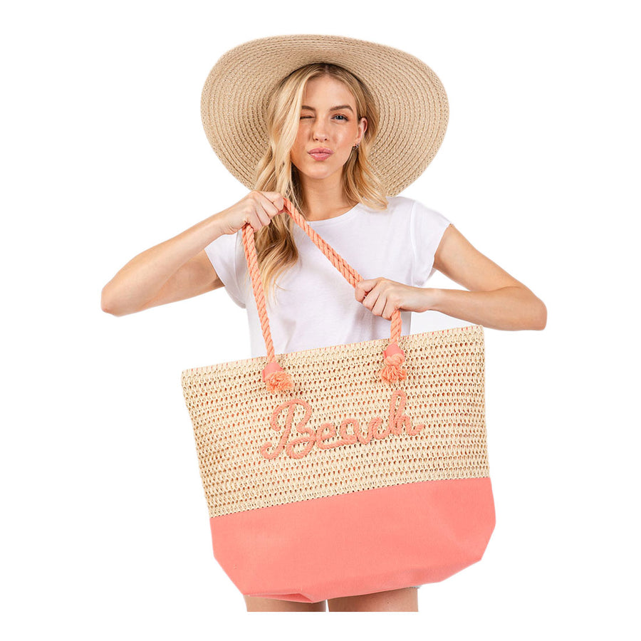 Woman holding a straw beach bag with coral bottom and pink handles on a white background